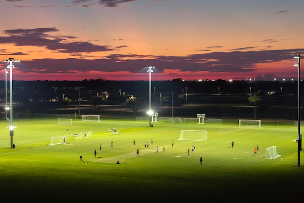 Pessoas jogando futebol em um estádio público iluminado ao pôr do sol Conceito de estilo de vida ativo