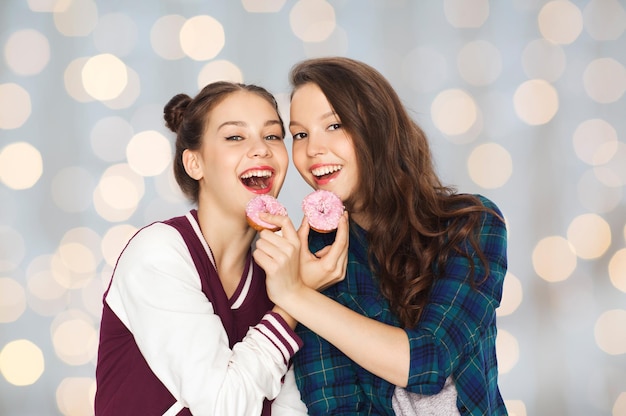 pessoas, junk food, adolescentes e conceito de amizade - felizes sorrindo muito adolescentes com rosquinhas comendo e se divertindo durante as férias luzes de fundo