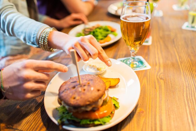 pessoas, lazer, amizade, alimentação e conceito de comida - close-up das mãos de amigos com hambúrguer no bar ou pub