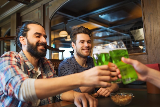 Foto pessoas lazer e st patrick dia conceito felizes amigos do sexo masculino beber cerveja verde e trocar copos no bar ou pub