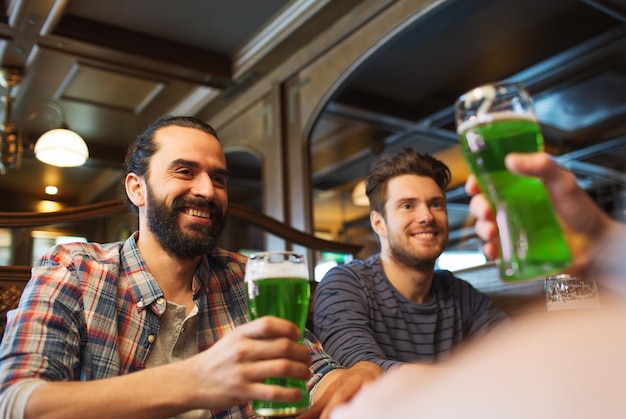 Pessoas lazer e st patrick's day conceito felizes amigos do sexo masculino bebendo cerveja verde no bar ou pub