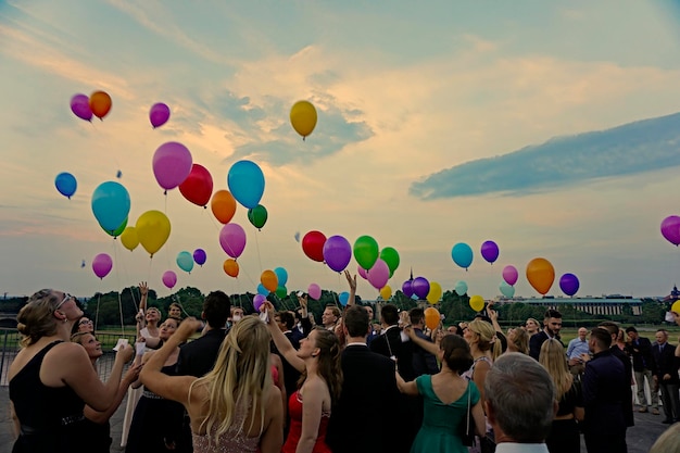 Pessoas liberando balões multicoloridos na festa de formatura durante o pôr do sol