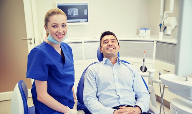 pessoas, medicina, estomatologia e conceito de saúde - dentista feminina feliz com paciente homem no consultório da clínica odontológica