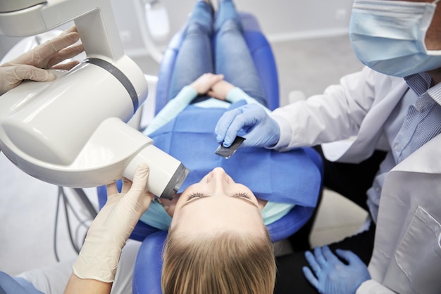 pessoas, medicina, estomatologia, tecnologia e conceito de saúde - close-up do dentista colocando escudo intraoral na boca do paciente feminino e assistente dirigindo a máquina de raio-x na clínica odontológica