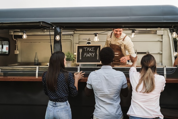 Pessoas multirraciais pedindo comida no balcão de um food truck ao ar livre - foco na placa de take away