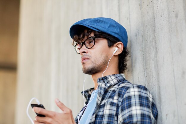 pessoas, música, tecnologia, lazer e estilo de vida - homem jovem hipster feliz com fones de ouvido e smartphone ouvindo música