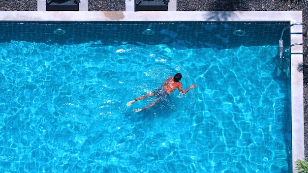 Pessoas nadando no ângulo de visão superior da piscina que têm água de cor azul e luz do sol refletem na superfície.