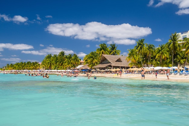 Pessoas nadando perto da praia de areia branca com bar de bangalô de guarda-chuvas e palmeiras de coco mar turquesa do Caribe Ilha de Isla Mujeres Mar do Caribe Cancun Yucatan México