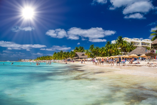 Pessoas nadando perto da praia de areia branca com bar de bangalô de guarda-chuvas e palmeiras de coco mar turquesa do Caribe Ilha de Isla Mujeres Mar do Caribe Cancun Yucatan México