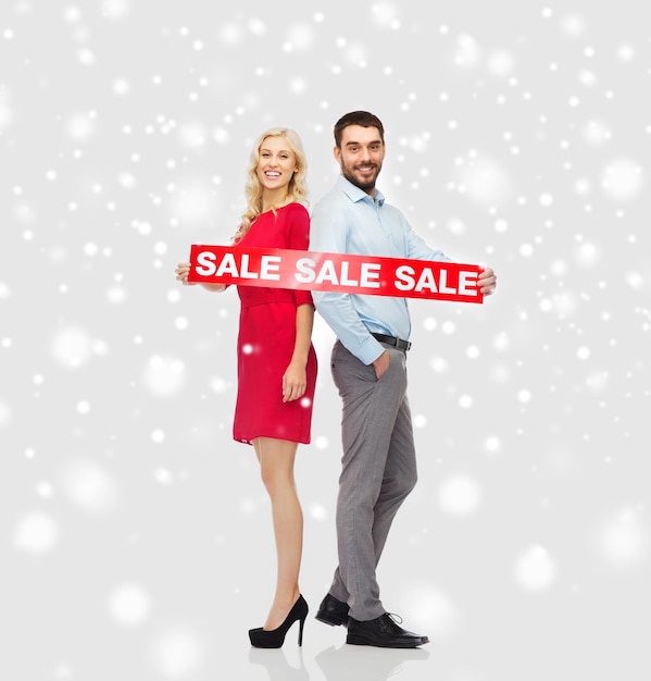 pessoas, natal, compras, inverno e conceito de férias - casal feliz com sinal vermelho de venda sobre fundo de neve