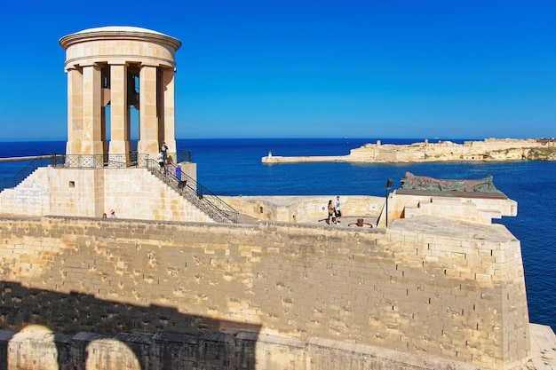 Pessoas no memorial Siege Bell no bastião de St Christopher em Grand Harbour, Valletta, Malta