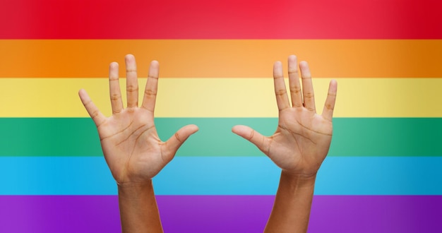 pessoas, orgulho gay e conceito homossexual - palmas de mãos humanas afro-americanas sobre fundo de listras de bandeira de arco-íris