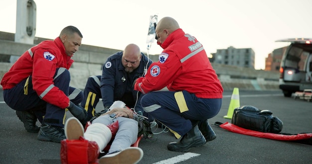 Pessoas paramédicas e ajudam o paciente na estrada no local para resgate de emergência e apoio equipe de paramédicos cuidados de saúde e camisa para pessoa ferida em acidente com cuidados de serviço médico e saco IV