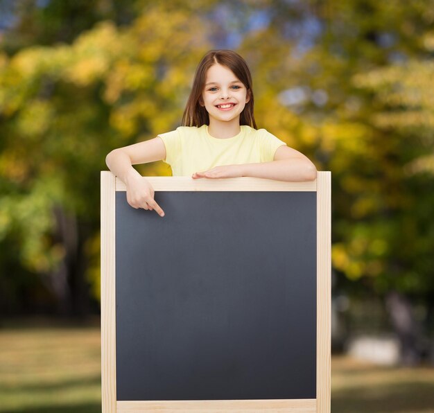 pessoas, propaganda e conceito de educação - menina feliz apontando o dedo para o quadro-negro