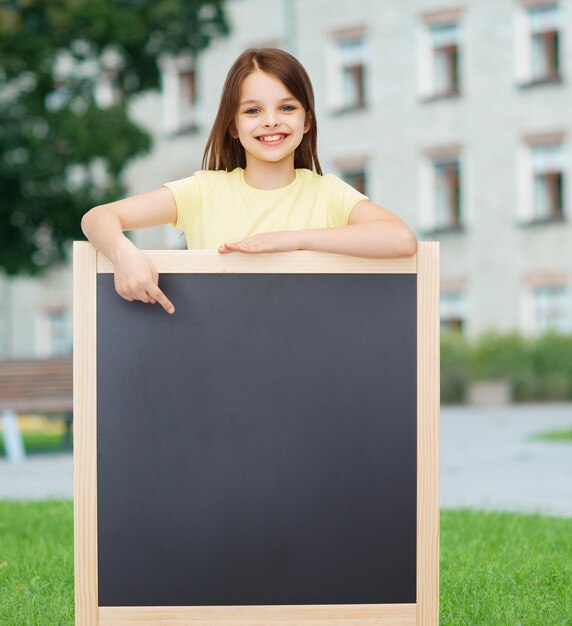 pessoas, propaganda e conceito de educação - menina feliz apontando o dedo para o quadro-negro