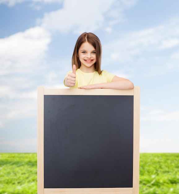 pessoas, propaganda e conceito de educação - menina feliz com quadro-negro em branco mostrando os polegares