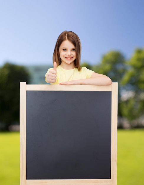 pessoas, propaganda e conceito de educação - menina feliz com quadro-negro em branco mostrando os polegares