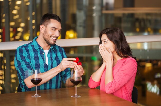 Foto pessoas, proposta, amor, casal e conceito de férias - homem sorridente dando anel de noivado de diamante para sua namorada feliz no restaurante