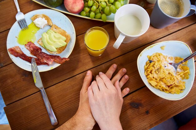 Foto pessoas relações e conceito de alimentação casal multirracial de mãos dadas enquanto toma café da manhã em uma mesa cheia de comida
