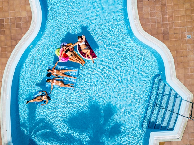 Pessoas se divertindo no verão na piscina com colchões infláveis coloridos da moda