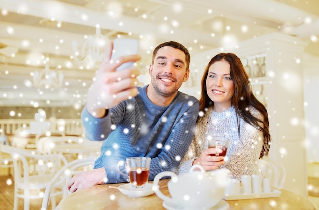 pessoas, tecnologia e conceito de namoro - casal feliz tirando selfie de smartphone e bebendo chá no café ou restaurante