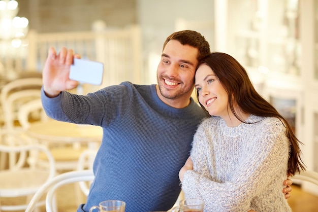 Foto pessoas, tecnologia e conceito de namoro - casal feliz tirando selfie de smartphone no café ou restaurante