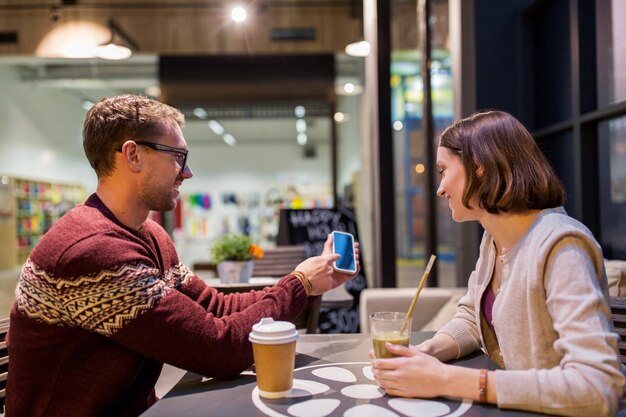 pessoas, tecnologia, estilo de vida e conceito de namoro - casal feliz com smartphone bebendo café e smoothie no café