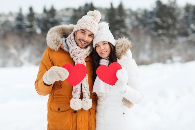 pessoas, temporada, amor e conceito de dia dos namorados - casal feliz segurando corações vermelhos em branco sobre a paisagem de inverno