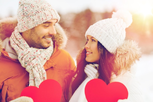 pessoas, temporada, amor e conceito de dia dos namorados - casal feliz segurando corações vermelhos em branco sobre a paisagem de inverno