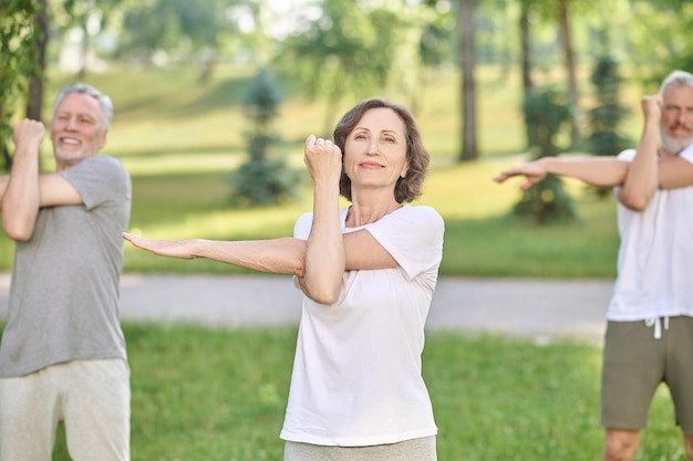 Pessoas tendo uma aula de ioga no parque e esticando os braços