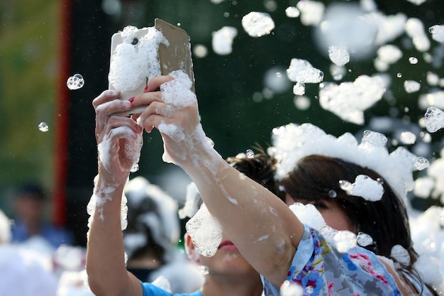 Pessoas tiram uma selfie com um telefone celular em espuma com sabão em um show