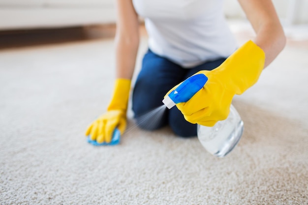 pessoas, trabalho doméstico e conceito de limpeza - close-up de mulher em luvas de borracha com pano e spray derergent limpeza tapete em casa