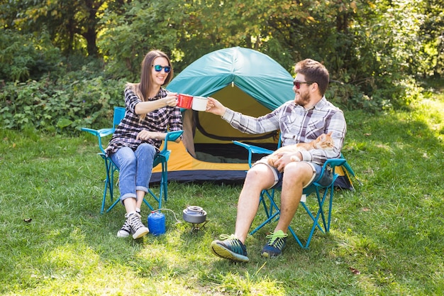 Pessoas, turismo de verão e conceito de natureza - jovem casal sentado perto de uma tenda.