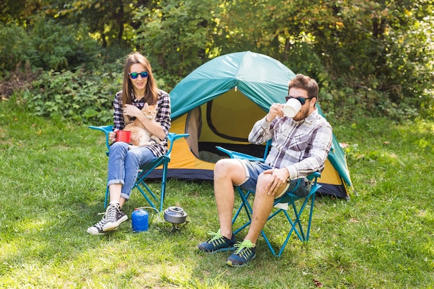 Pessoas, turismo de verão e o conceito de natureza - jovem casal bebendo chá perto da tenda.