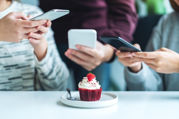 Pessoas usando telefone celular para tirar uma foto de um cupcake antes de comer no café