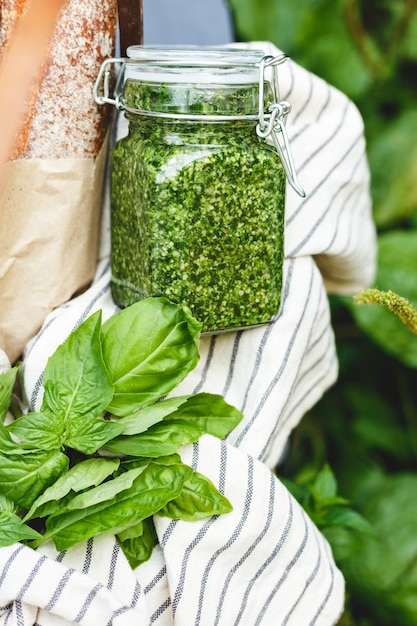 Pesto casero en un frasco de vidrio con albahaca, ajo, pan al aire libre en una canasta. Cesta de picnic con salsa pesto para preparar pan de ajo o bruschetta. Salsa tradicional italiana - Pesto.