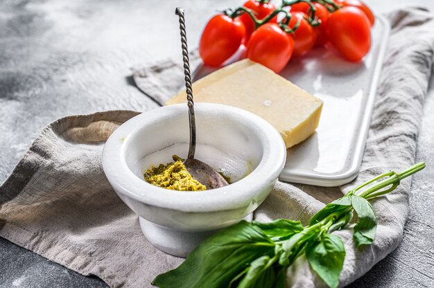 Pesto casero en mortero de mármol, hojas de albahaca y parmesano en una tabla de cortar.