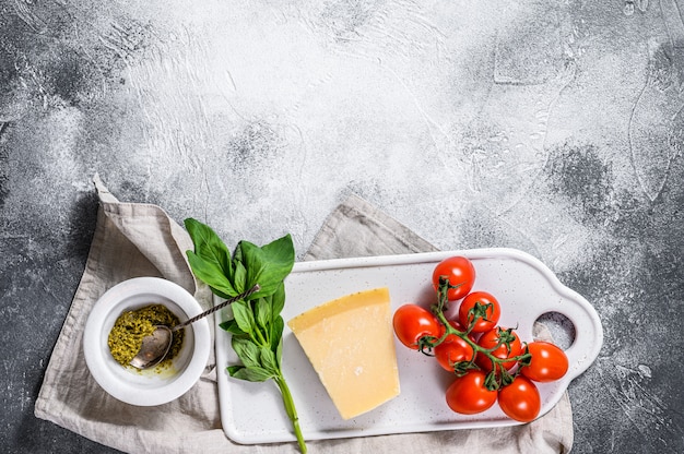 Pesto em argamassa de mármore, folhas de manjericão e parmesão em uma tábua.