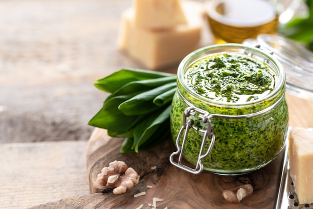 Pesto de puerros silvestres con aceite de oliva y queso parmesano en un frasco de vidrio sobre una mesa de madera. Propiedades útiles de ramson. Hojas de ramson fresco. Copia espacio