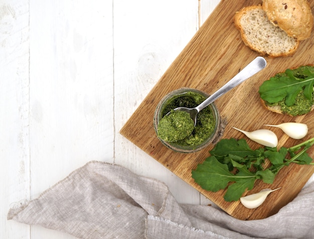 pesto de rúcula en un frasco y hojas de rúcula honestidad y tostadas se encuentran una al lado de la otra