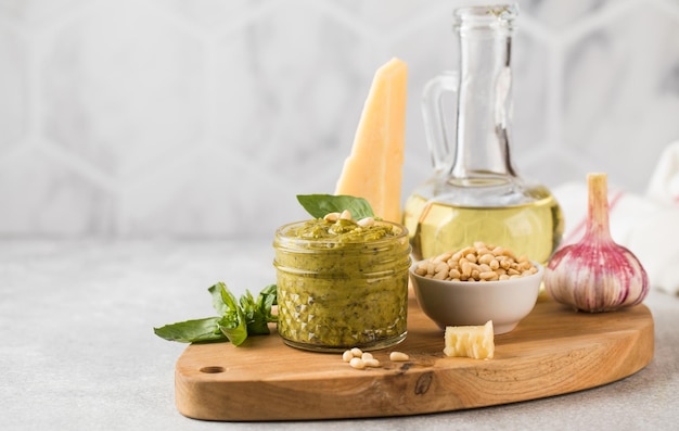 Pesto-Sauce in einem Glas mit einem Stück Parmesan Basilikumblätter Pinienkerne und Olivenöl in einer Flasche italienische Küche