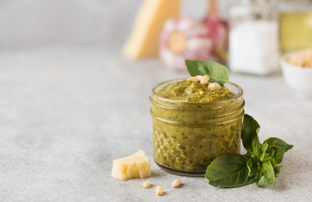 Pesto-Sauce in einem Glas mit Pinienkernen, einer Scheibe Parmesan und grünen Basilikumblättern Kopieren Sie Platz