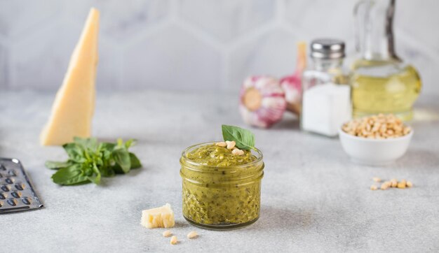 Pesto-Sauce in einem Glas mit Pinienkernen, einer Scheibe Parmesan und grünen Basilikumblättern Kopieren Sie Platz
