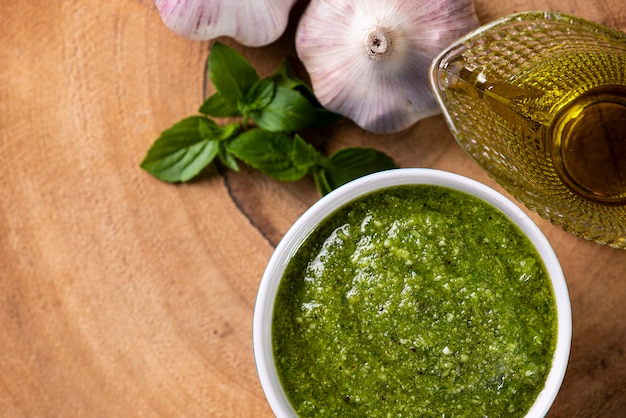 Pesto-Sauce. In einem transparenten Glas mit den Zutaten im Hintergrund. Olivenöl, Knoblauch und Basilikum.