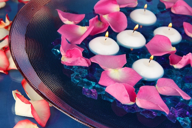 Pétalas de rosa e velas em água em vaso em close de fundo azul
