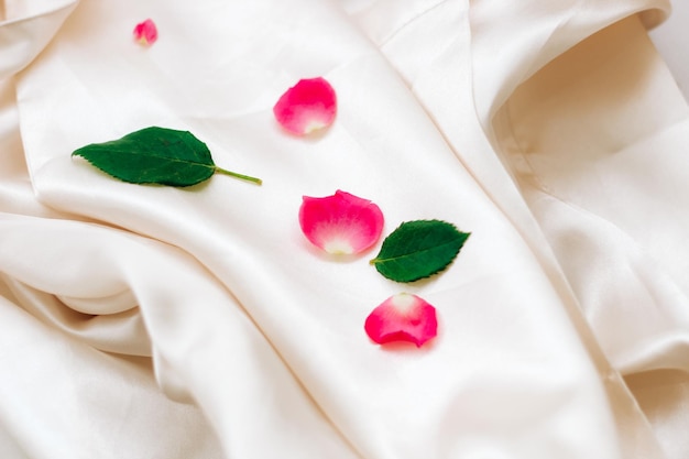 Pétalas de rosas cor de rosa em um fundo de seda branco com espaço para texto