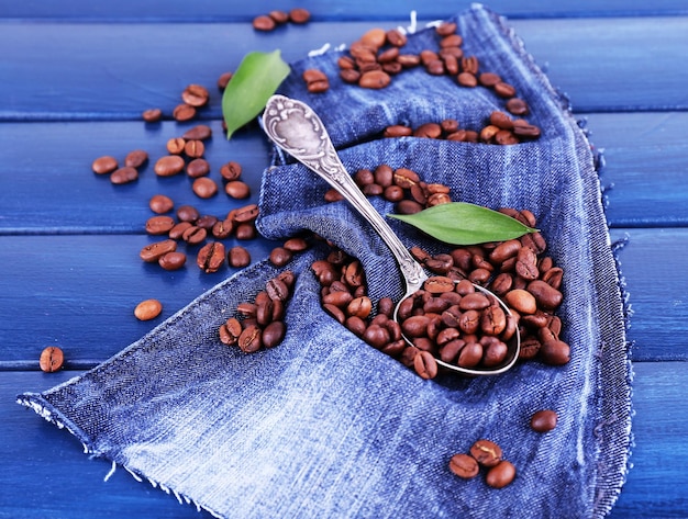 Pétalas verdes perto da colher de grãos de café sobre fundo azul de madeira com material jeans