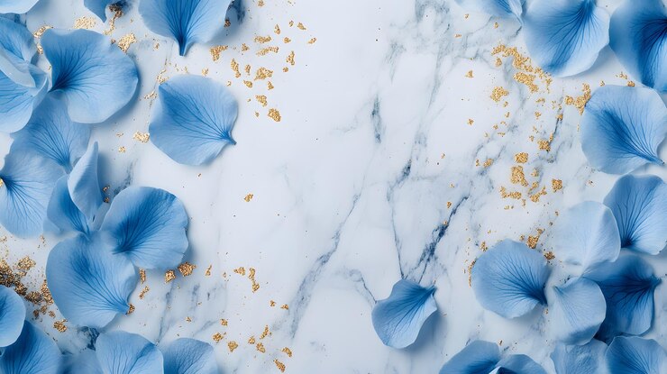 Pétalos de flores azules esparcidos sobre una superficie de mármol con brillo dorado