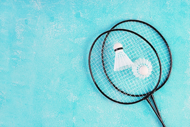 Peteca e raquetes de badminton em um fundo azul. vista do topo