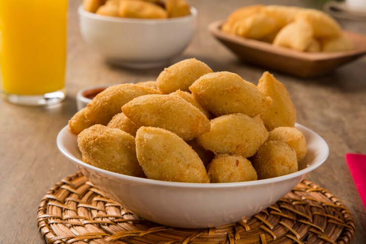Foto petisco brasileiro frito com presunto de queijo em fundo de madeira.